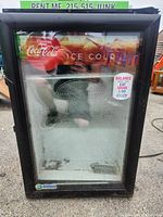 Front view of the Coca-Cola branded glass display fridge showing the black frame and logo on the glass door.