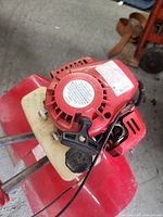 Close-up of the gas tiller’s pull-start engine with red housing and beige fuel tank.