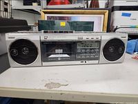 Front view of silver General Electric radio cassette player showing speakers, cassette compartment, and digital display with controls.