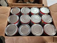 Box with 12 gel flame fireplace fuel cans with sealed metal lids viewed from above.