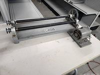 Side angled photo of Gemlap rock tumbler showing metal base, two rollers, motor, and drive wheel with attached wires.