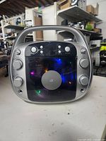 Front view of silver GPX karaoke player showing control buttons and illuminated CD cover.