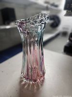 Side view of a tall, clear handblown glass vase with vertical ribs and ruffled top edge showing subtle pink and green coloring.