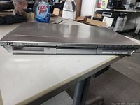 Front view of the silver JVC DVD player showing the logo, buttons, and disc tray before it is opened.