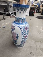 Full side view of ceramic vase showing floral blue and pink flower motifs, white background, and decorative blue top edge.