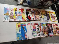 Photo showing 14 Mad magazines laid out in two rows on a white surface, covers visible