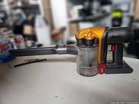 Dyson mini handheld vacuum with narrow nozzle attachment shown on table, dust container partially filled.
