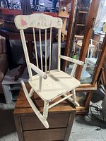 Full view of the vintage child's rocking chair showing white paint and decorative illustrations with visible wear