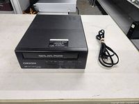 Front view of Orion VHS player and power cord on white surface.