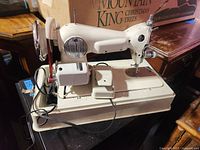 Full view of portable sewing machine with base and attached motor running on a table.