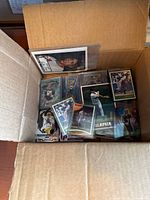 Open cardboard box filled with assorted sports trading cards in protective sleeves