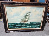 Full view of the framed oil on canvas ship painting showing a large sailing ship on the ocean with cloudy sky background.