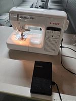 White Singer Quantum DSX sewing machine with foot pedal placed on table, powered on with light.