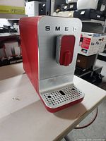 Front view of the Smeg red coffee machine with silver front panel and coffee lever.