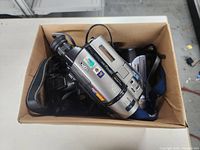 Box viewed from above showing silver Sony Handycam digital/analog video cameras along with cables in cardboard box.