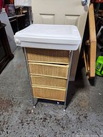 Front view of vintage baby changing table with white plastic flip-top and three wicker drawers