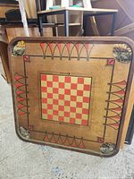 Wooden square game board featuring red and beige checkerboard center and red/black decorative arches along edges, showing wear and patina.