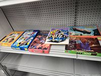 Shelf display of six vintage jigsaw puzzles with visible colorful illustrated box covers showing various themes including sci-fi and vehicles.