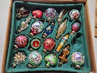 Top-down image showing 17 assorted vintage glass Christmas ornaments arranged inside green felt-lined wooden box.