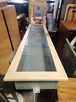 Top view showing the full length of the wall-mounted horizontal display cabinet with a wooden frame and glass top.