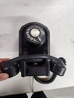 Top view of black rotary dial telephone showing base and handset cradle with coiled cord