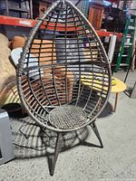 Front angled view of the wicker style patio egg chair showing the open weave design and the missing bolt on one leg.