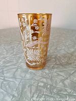 Front view of marigold carnival glass tumbler showing white enamel daisy pattern