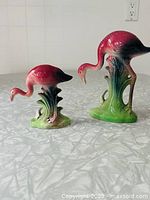 Both flamingo figurines side by side highlighting size difference and overall appearance