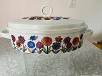 Side view of casserole on stand showing floral design and loop handle lid