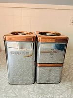 Front view of Sugar and Tea canisters stacked with Coffee, shows chrome bodies and copper lids