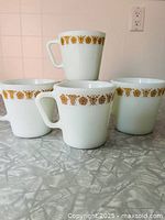 Four Pyrex Butterfly Gold mugs stacked and arranged