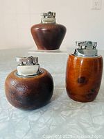 Front view of three wooden table lighters showing shapes and metal tops