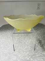 Side view of oval amber Depression Glass bowl with scalloped edges and pedestal feet on textured surface.