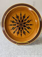 Full view of the round auburn ironstone plate with black starburst pattern at center and concentric brown rings on the rim with handle cut-out.