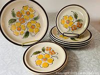 Group photo showing eight Montrose stoneware plates, four larger dinner plates and four smaller side plates, all with yellow and orange floral pattern and brown rims.
