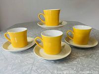 Four bright yellow teacups placed on off-white saucers arranged on a table.