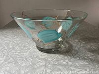 Clear glass chip bowl with turquoise leaf and gold pattern on a white textured surface, showing the bowl front angled upward.