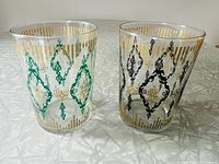 Pair of clear beverage glasses with damask patterns in teal and black with gold accents.