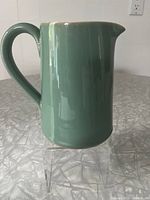 Front and side view of the green stoneware jug with handle and spout showing smooth matte glaze in Manor Green color.