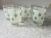 Four Dominion Glass frosted juice glasses with green starburst pattern and horizontal bands displayed on a table.