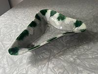 Triangular green and grey glazed ceramic dish on a textured surface showing top detail and shape.