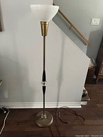 Full view of mid-century floor lamp showing milk glass shade, metal body, black accents, and power cord on hardwood floor.