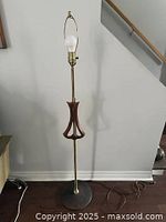 Full view of the mid-century standing floor lamp showing metal stand, wooden accent, base, bulb socket with harp and bulb.