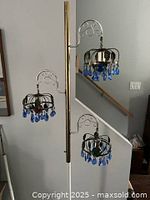 Full view of the floor lamp showing the gold-tone standing pole with three arms holding the light fixtures with blue teardrop crystals.