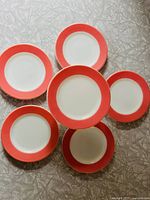 Top-down view of six round dishes arranged in a flower-like pattern showing the coral pink band and white center.
