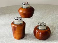 Three table lighters made of Bermuda Cedar wood with silver-toned metal lighter tops, two smaller and one larger item shown grouped on a reflective surface.