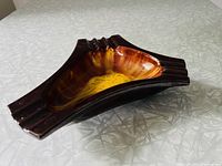 Side angle of a brown and golden yellow drip glazed ceramic ashtray with asymmetrical boomerang shape showing three cigarette rests on each end and glossy finish.