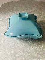 Top view of blue ceramic casserole dish lid with sculpted handle and abstract curved edges.