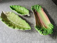 Three vintage ceramic serving dishes placed together showing lettuce leaf and rhubarb stalk shapes and coloring.