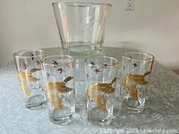 Set of four clear Dominion Glass beverage glasses decorated with gold Canadian geese in flight over marsh with additional small flying birds, arranged in front of a clear ice bucket.